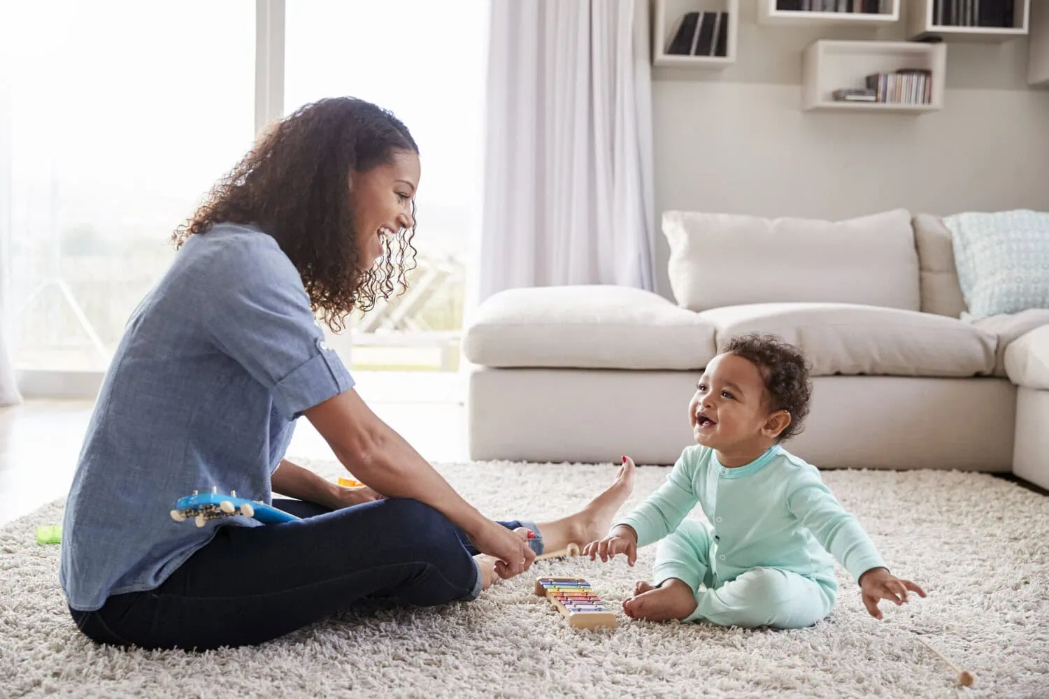 An adult plays with a toddler on the floor.