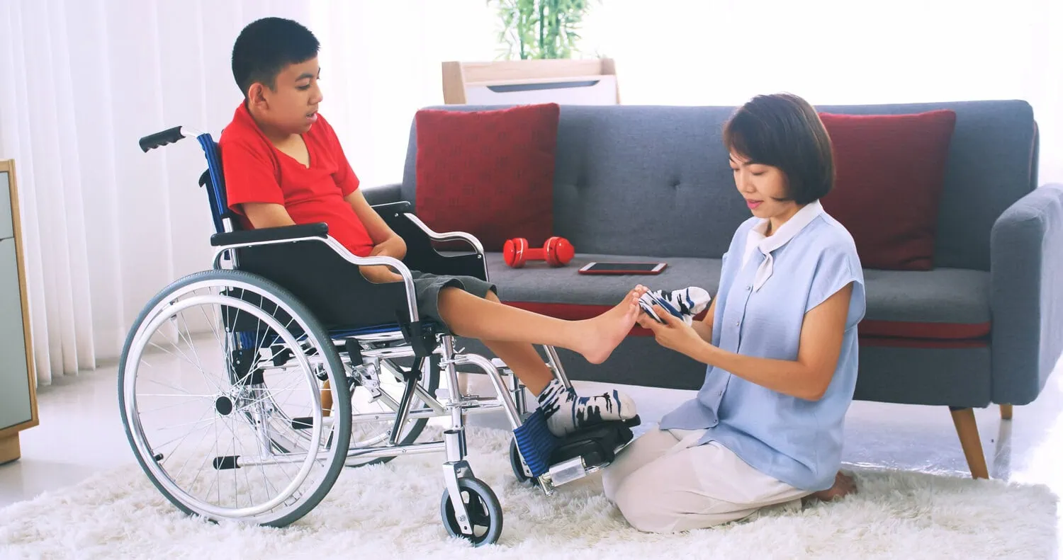 An adult supports a child in a wheelchair.