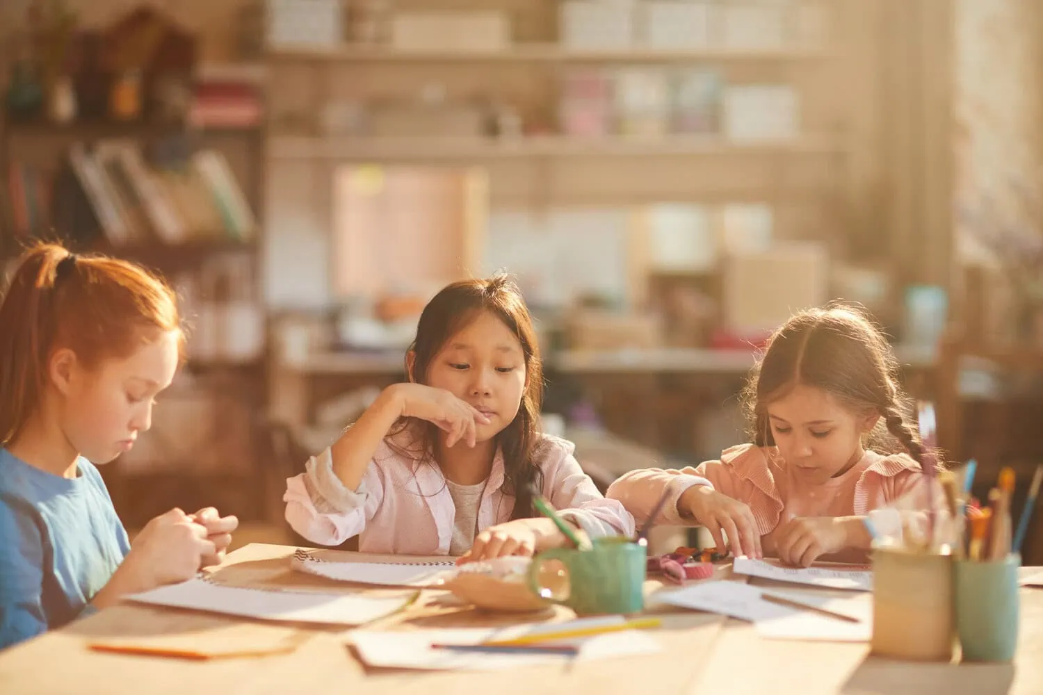 Three children draw together at a table.