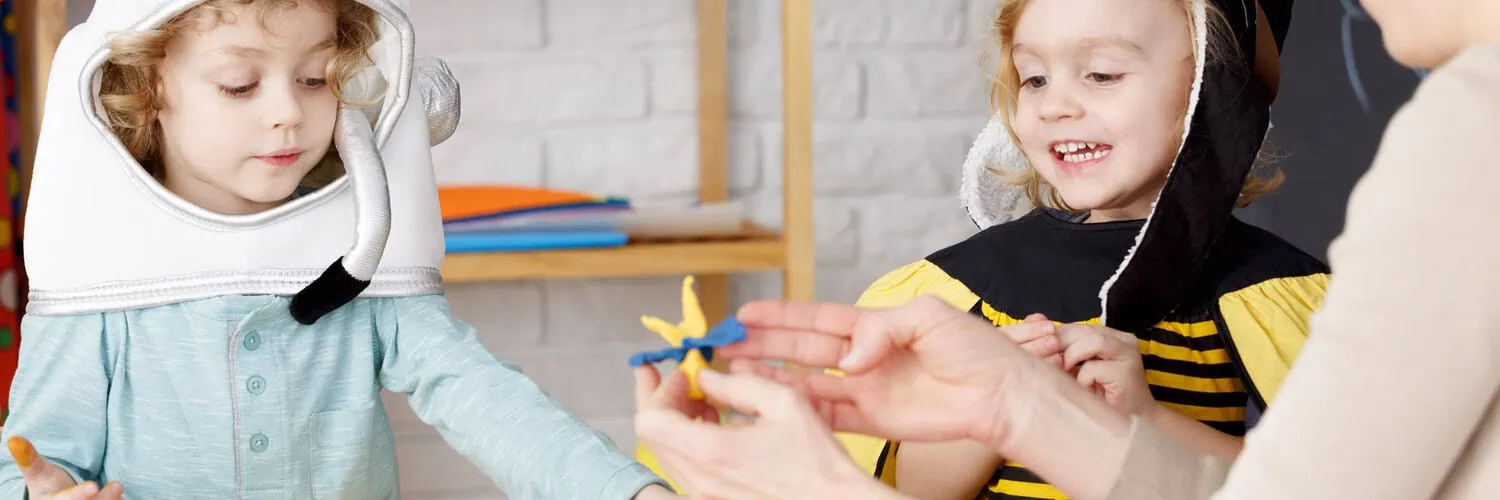 Two children in astronaut and bee costumes play with a toy.