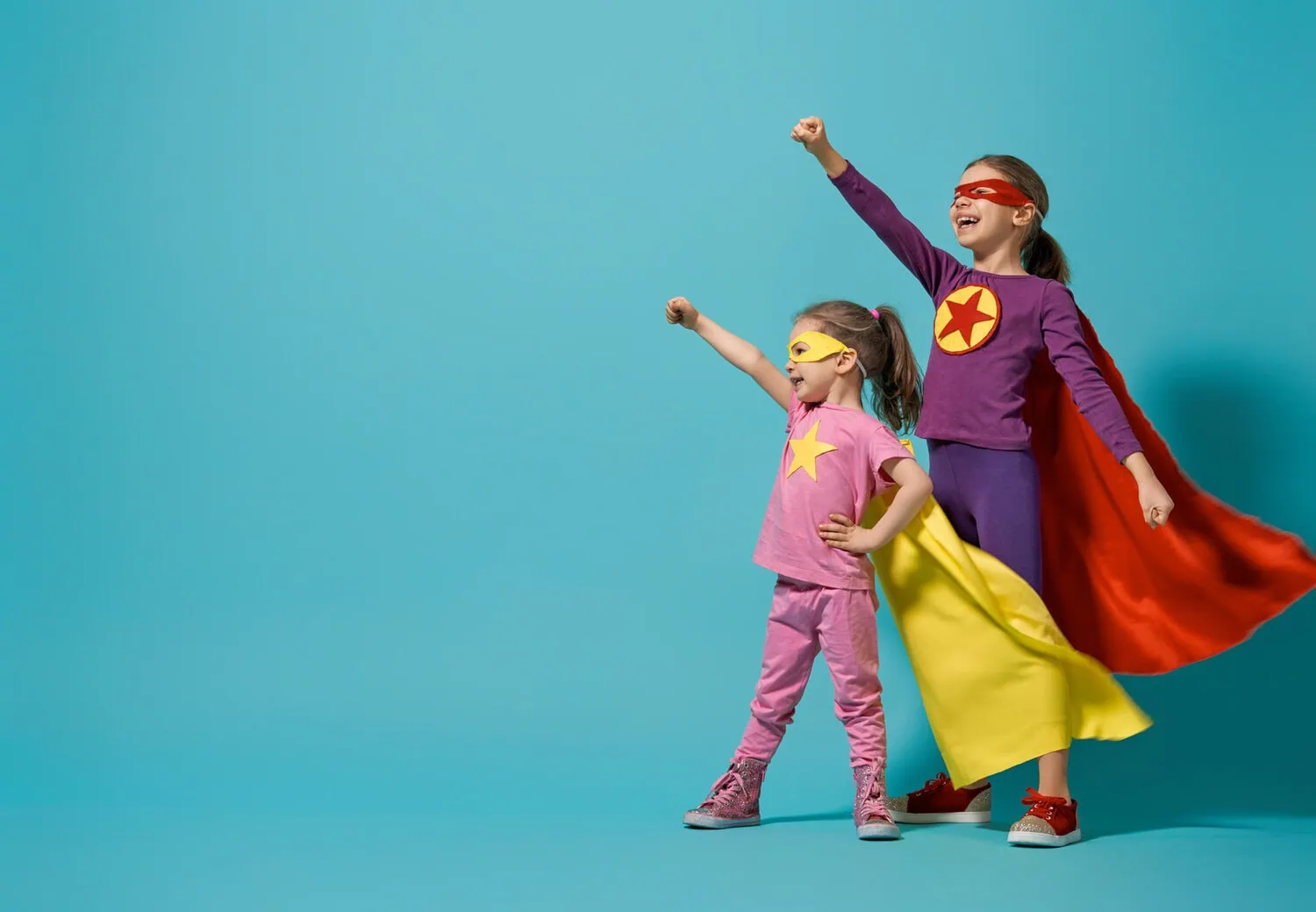 Two children wearing superhero costumes pose against a blue background.