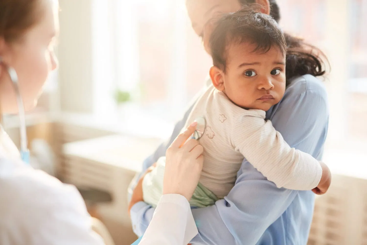 A doctor examines a child held by an adult.