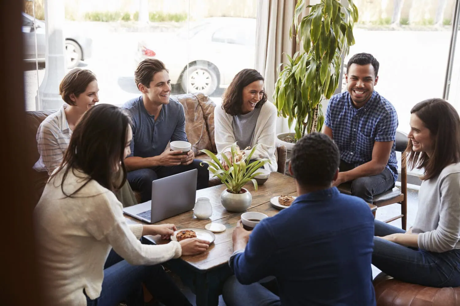 A group of adults gather around a table, talking over coffee.