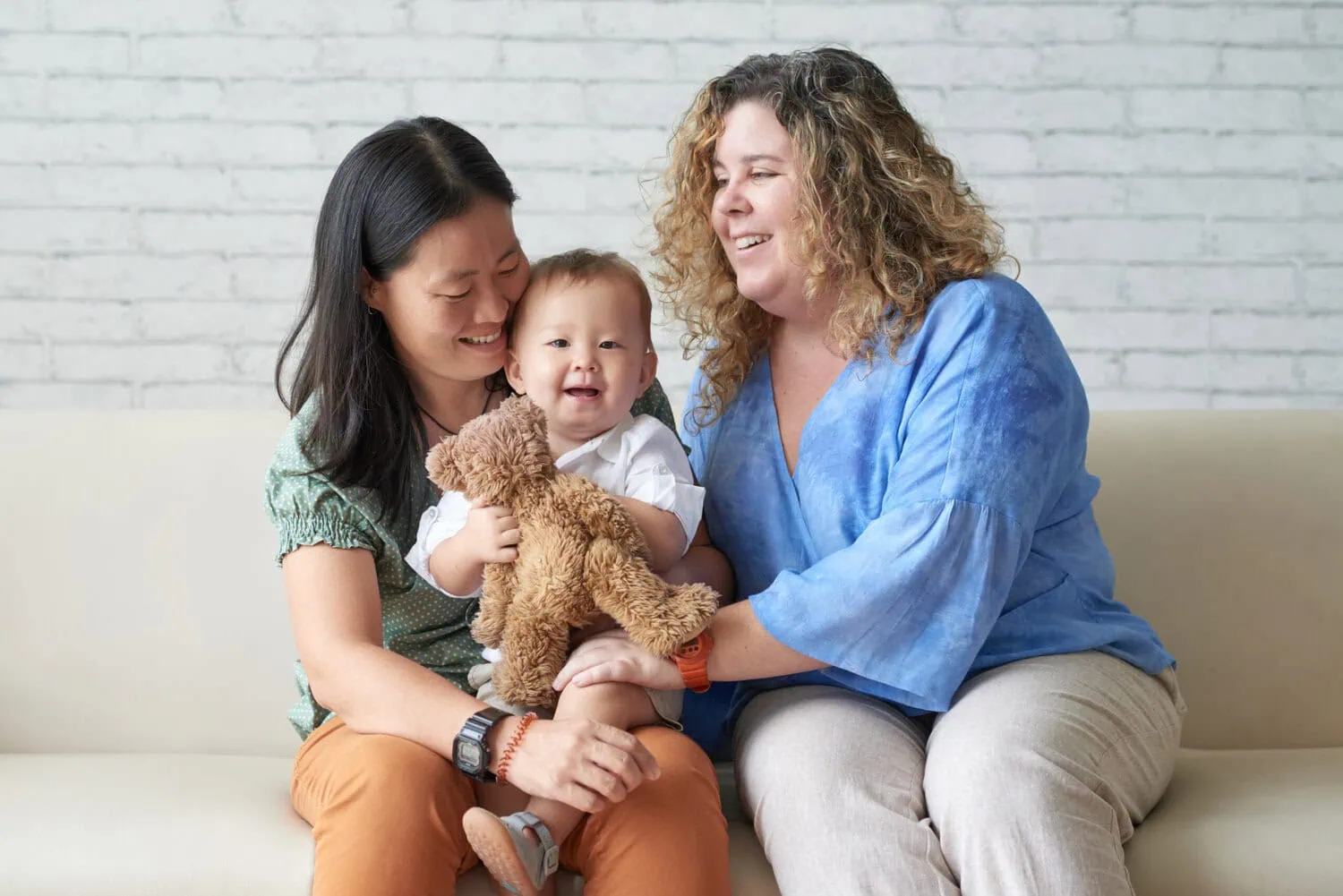 A lesbian couple sits with a baby on a couch.