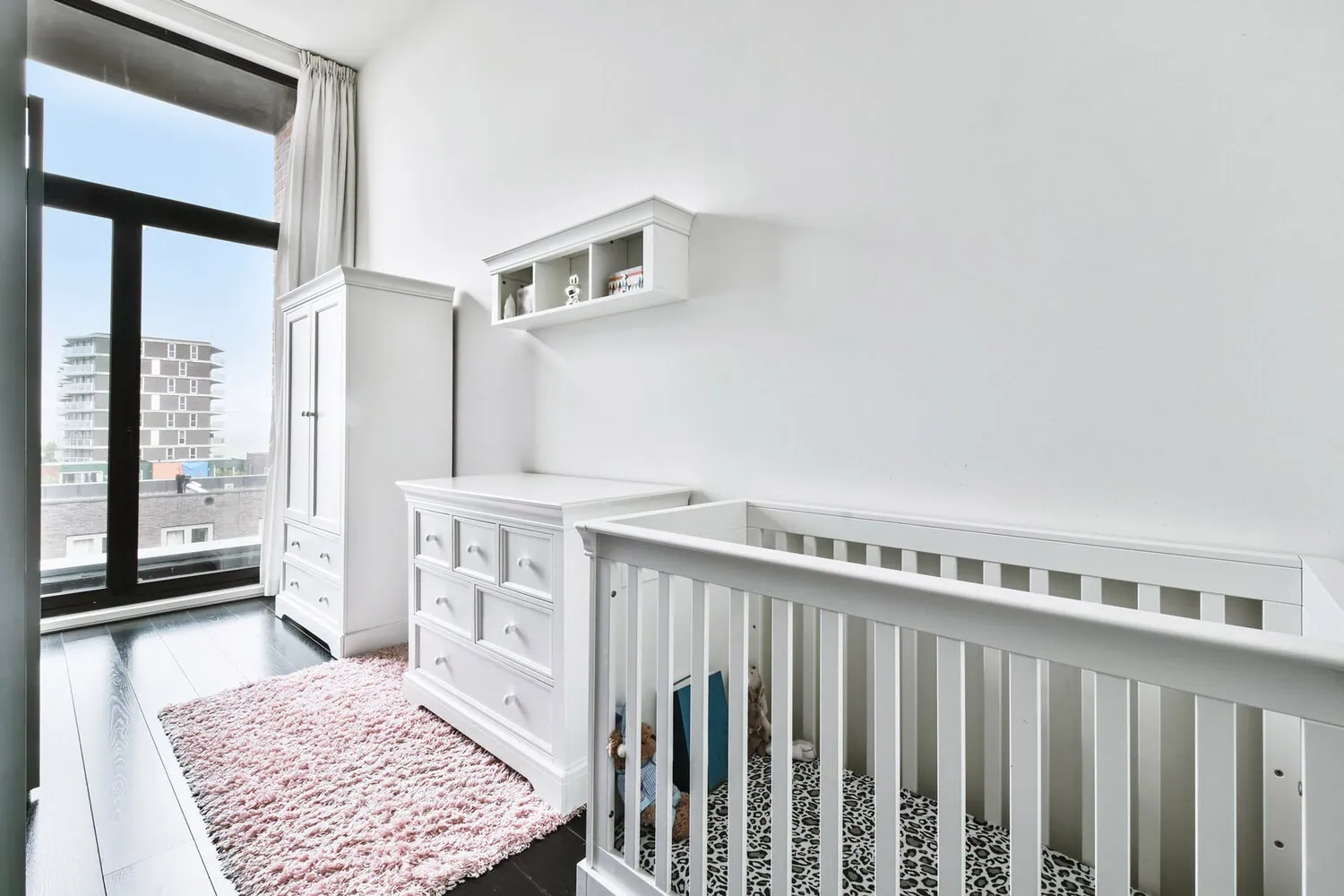 A bright nursery with a white crib, dresser, and storage shelves.