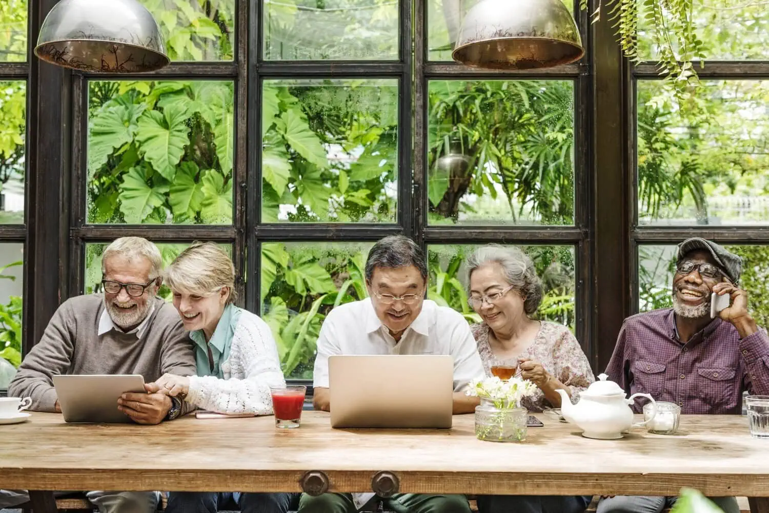Older adults sit together at a table using digital devices.