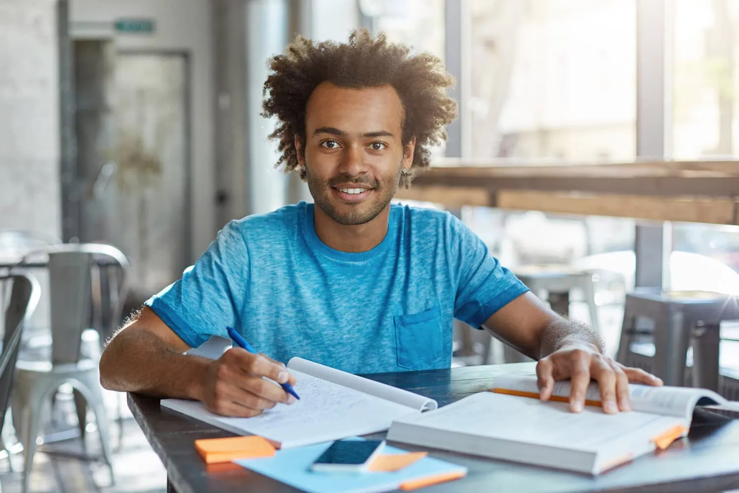 A student studies at a desk with books and papers.