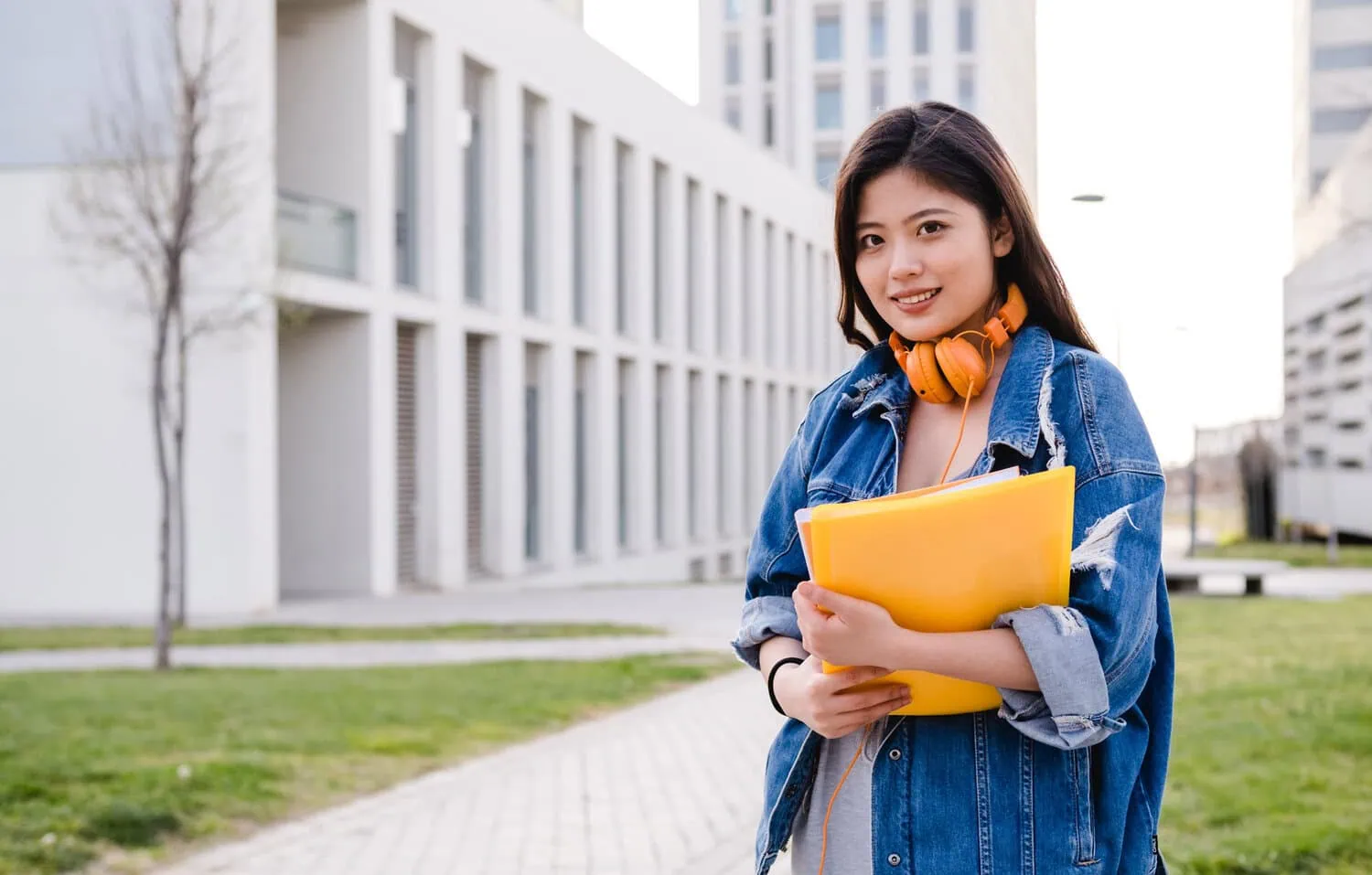A university student stands outdoors holding a folder.
