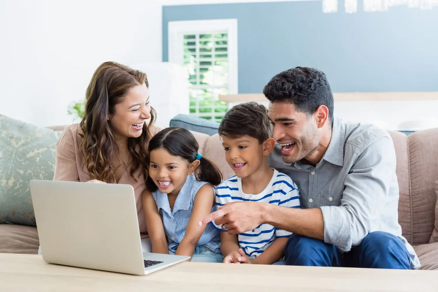 Two adults and two children use a laptop together in a living room.